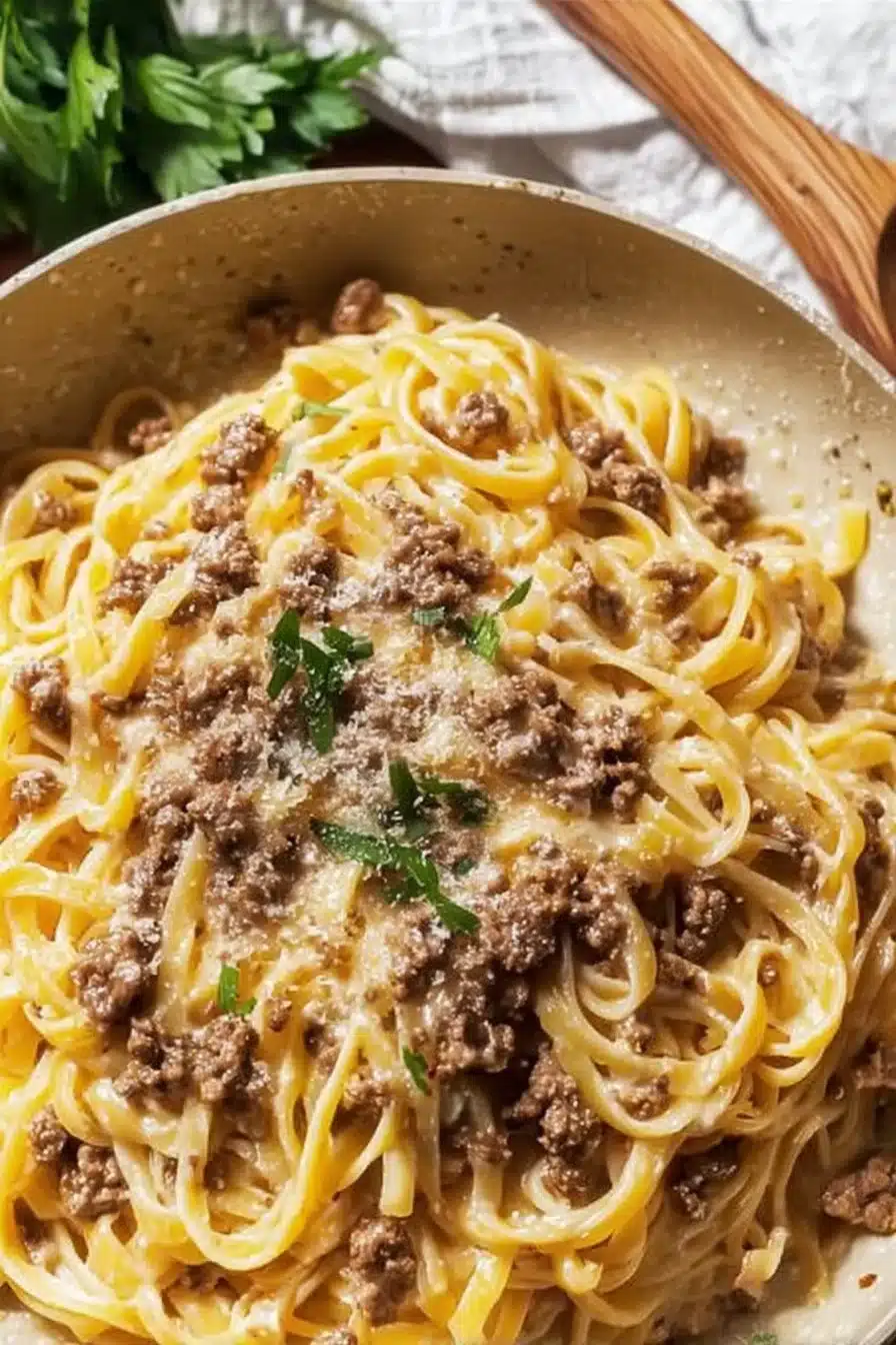 Creamy garlic butter pasta topped with ground beef in a white bowl.